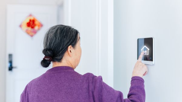 Mulher na terceira idade mexendo em painel de controle de casa inteligente para idosos